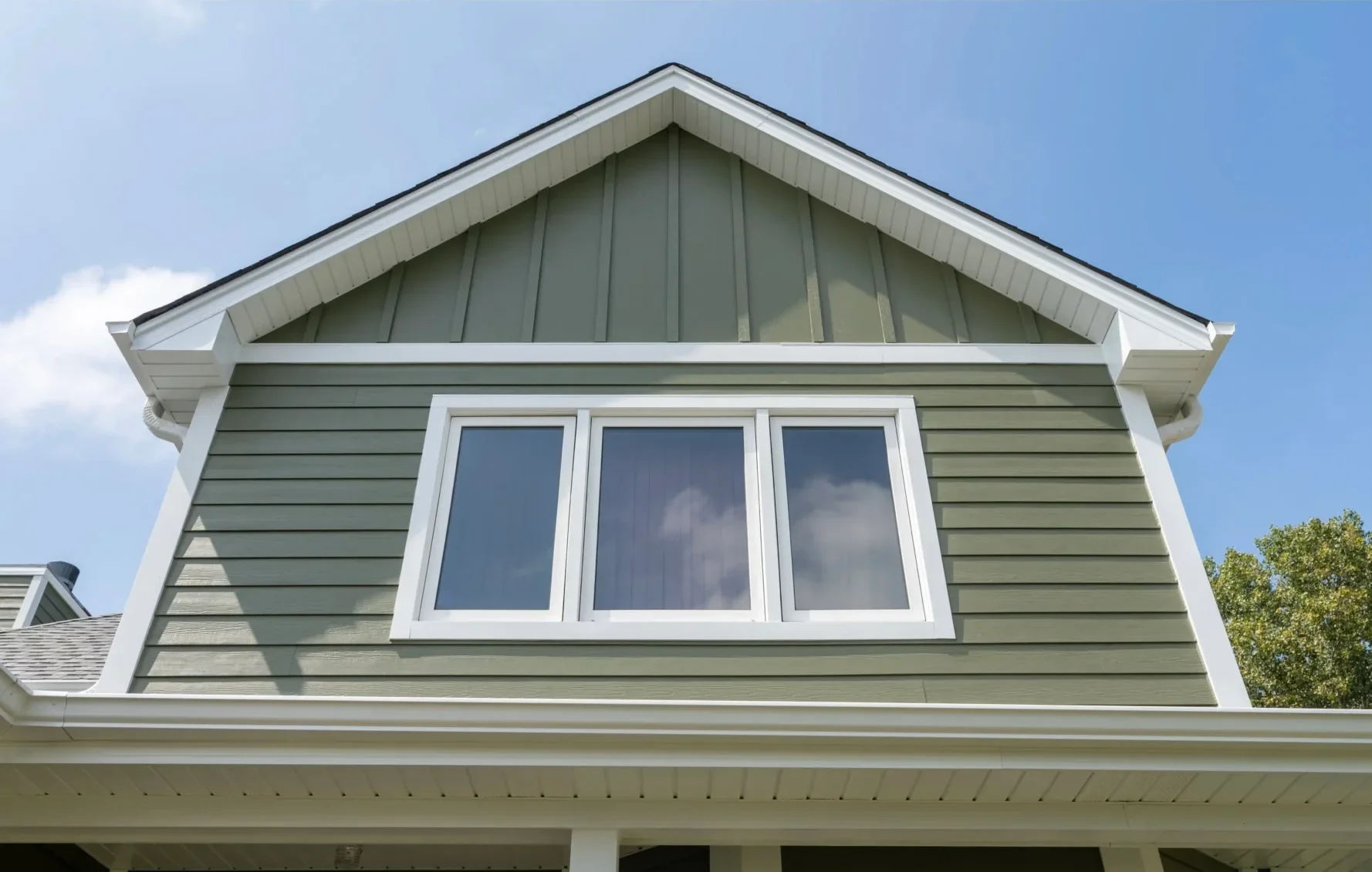 Sage green horizontal siding with white trim, three-window casement installation on gable end
